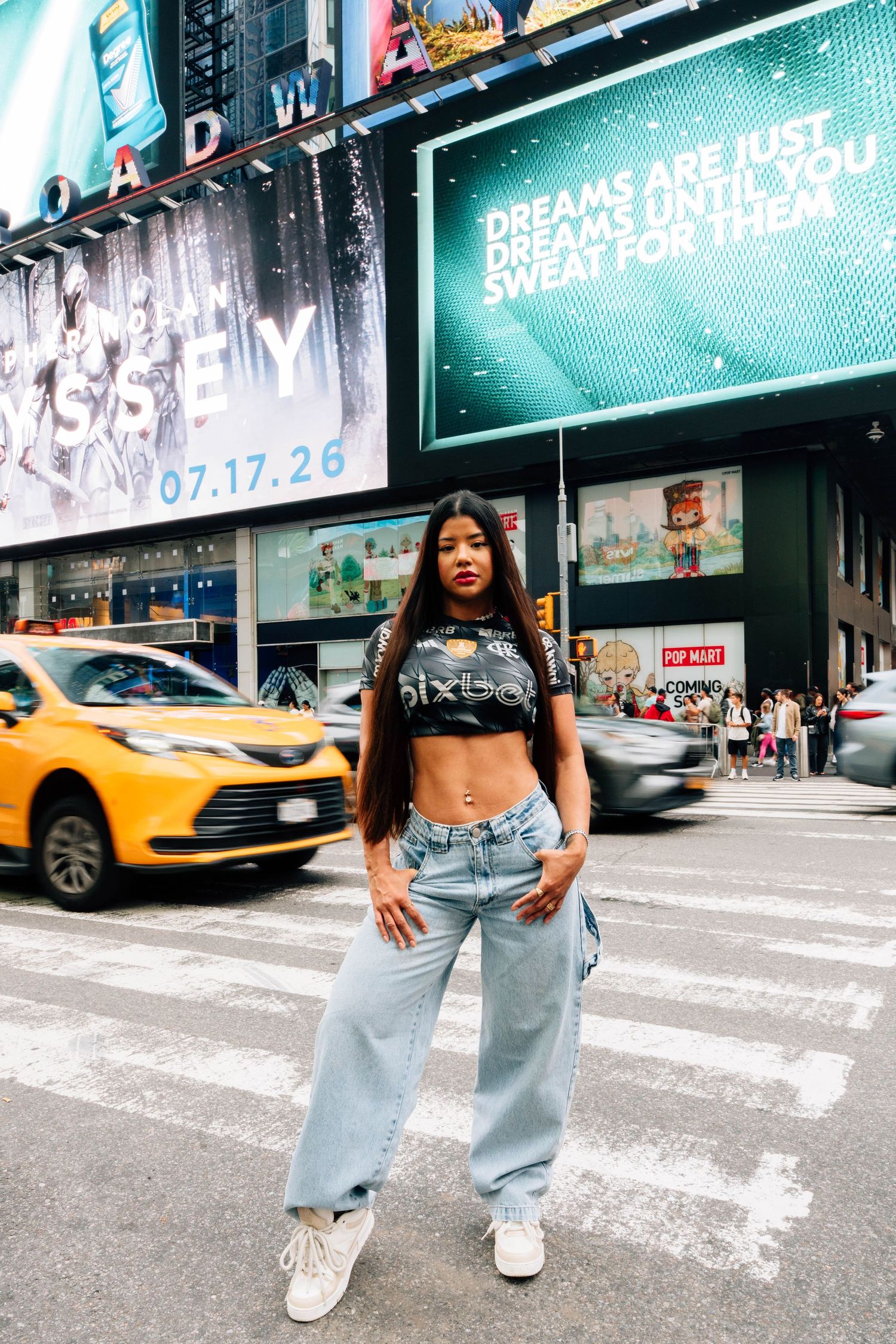 Young woman posing confidently at Times Square NYC in crop top and wide-leg jeans with Broadway billboards behind her.