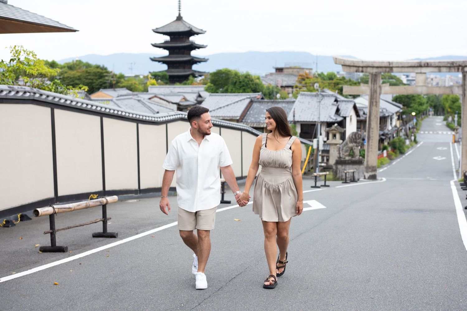 Couple holding hands walking down a quiet street in Kyoto, Japan, with a traditional pagoda and historic buildings in the background.