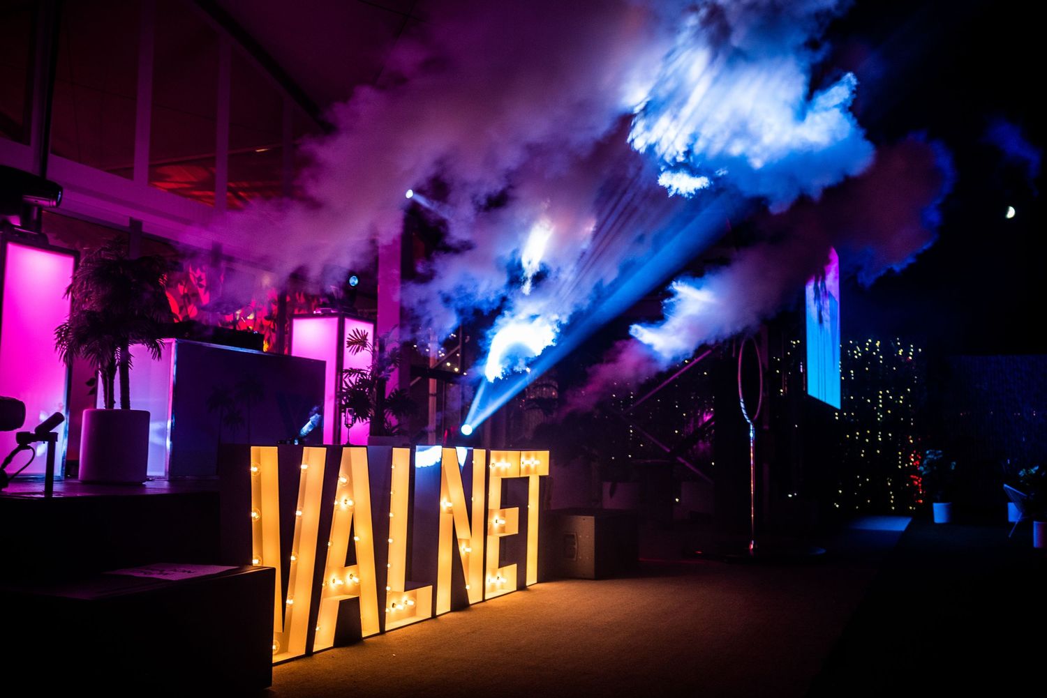 VALNET illuminated sign with colorful smoke and dramatic lighting at a vibrant indoor event.