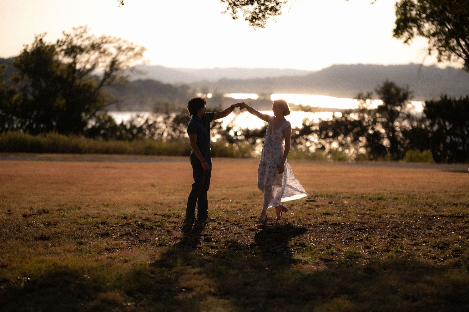 Couple dancing at sunset by a lake, silhouetted against golden light in a scenic outdoor setting.