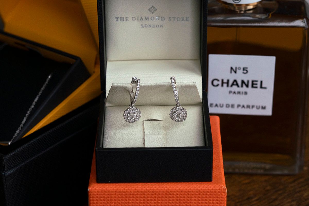 Wedding earrings in a presentation box beside Chanel No. 5 perfume and other bridal accessories.