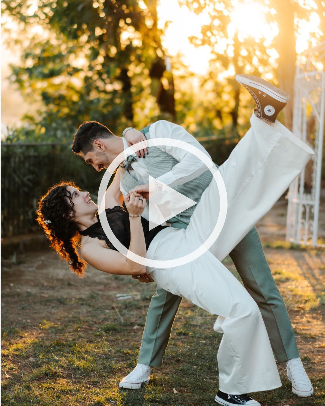 A groom dips his bride in a romantic sunset dance outdoors, she wears white while he wears sage green.