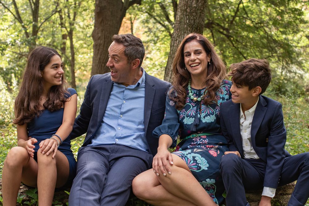 Happy family of four laughing together outdoors in a lush green forest setting.