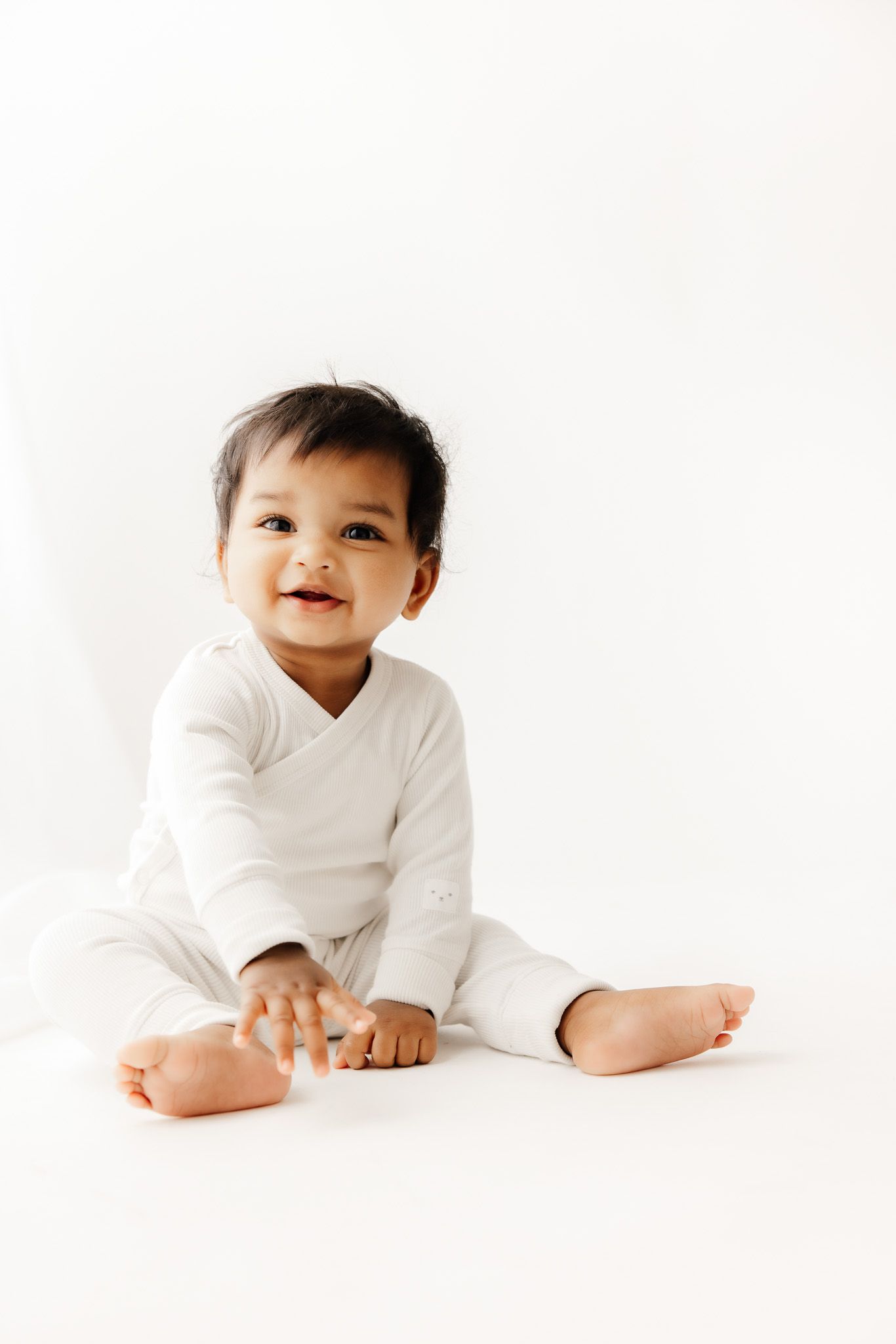 Peaceful newborn baby sleeping on white blanket, dark hair, soft skin, serene expression, professional newborn photography.