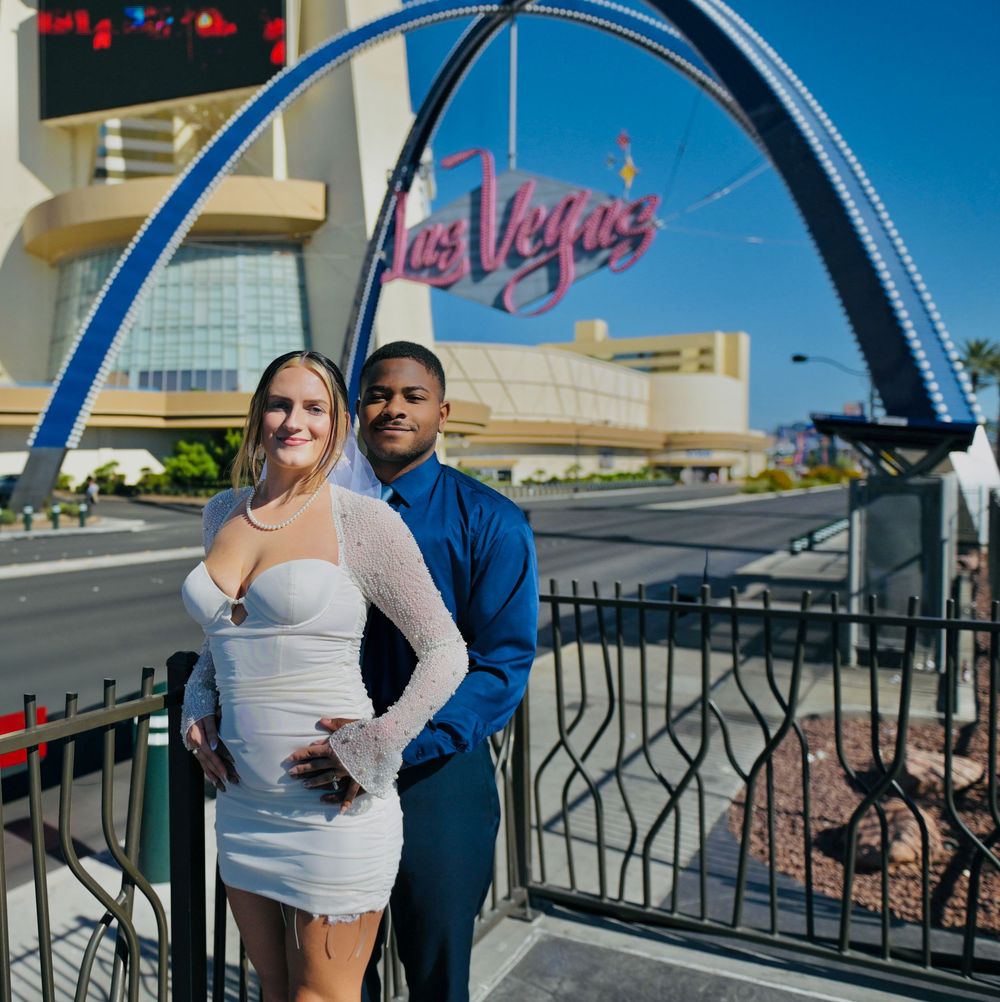 Couple in white dress and blue shirt pose by the iconic Las Vegas welcome arch with the neon sign on a sunny day.
