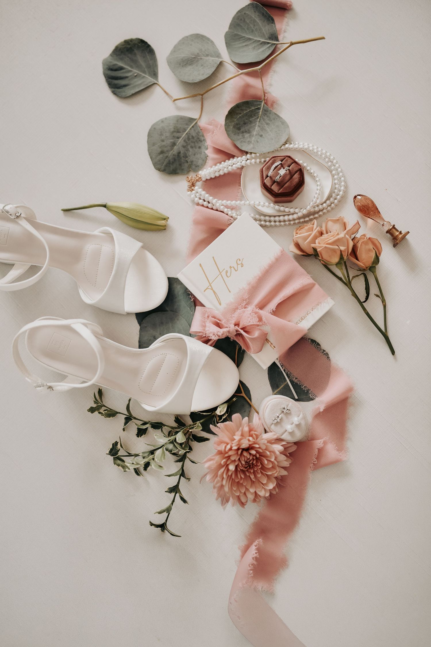 Romantic wedding flat lay featuring bridal jewelry, vow books and personalized details