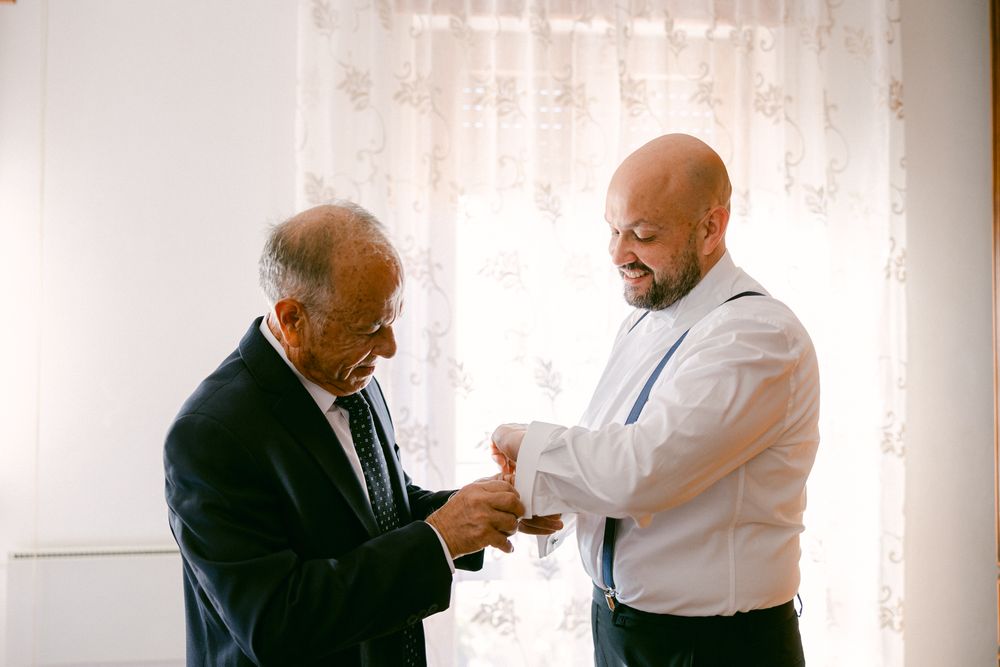 Una persona aiuta lo sposo a sistemare il polsino della camicia.