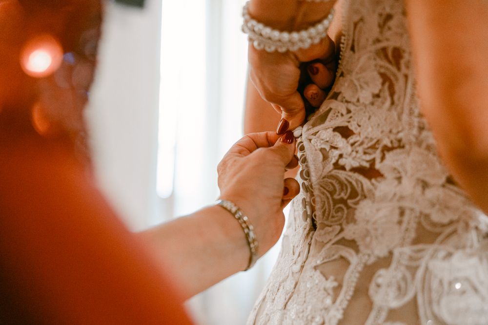 Mani che sistemano il corpetto dell’abito della sposa.