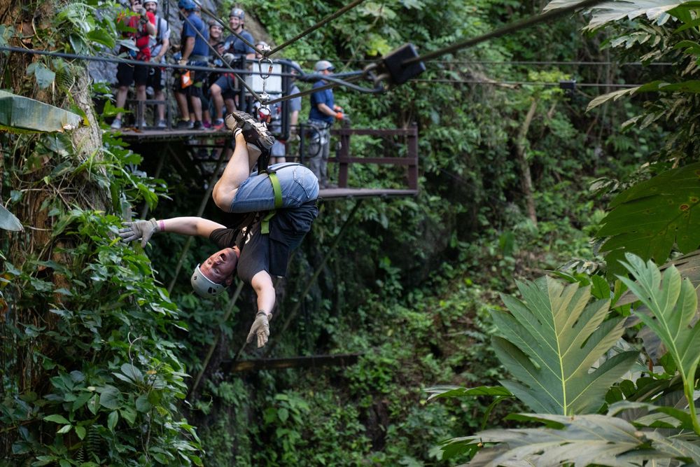 Person zip-lining upside down through a lush tropical jungle canopy.
