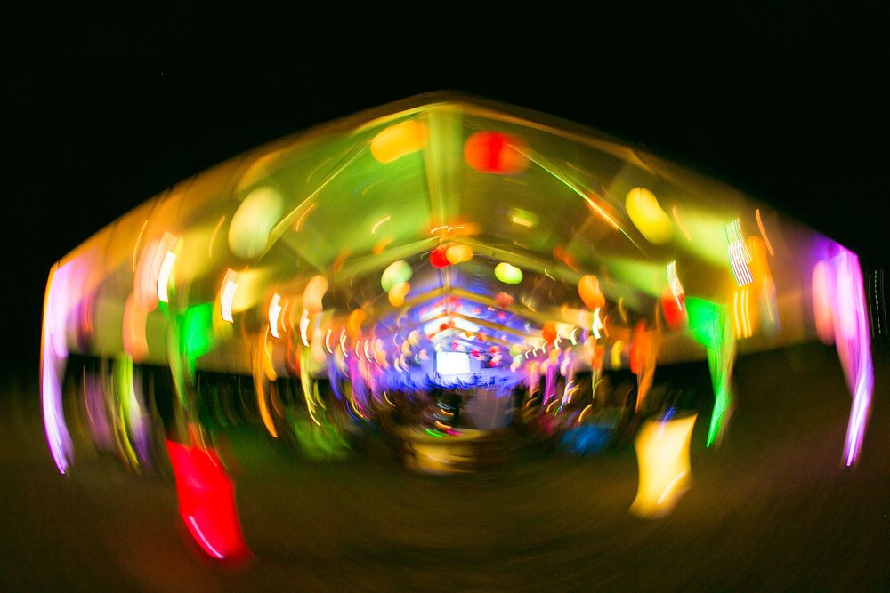 Colorful blurred neon lights creating a swirling tunnel effect at a nighttime carnival or festival.
