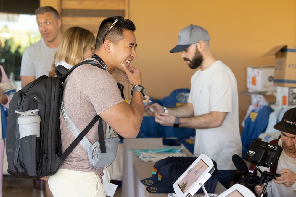 People networking at an outdoor event booth with cameras and tablets on display in a sunny setting.