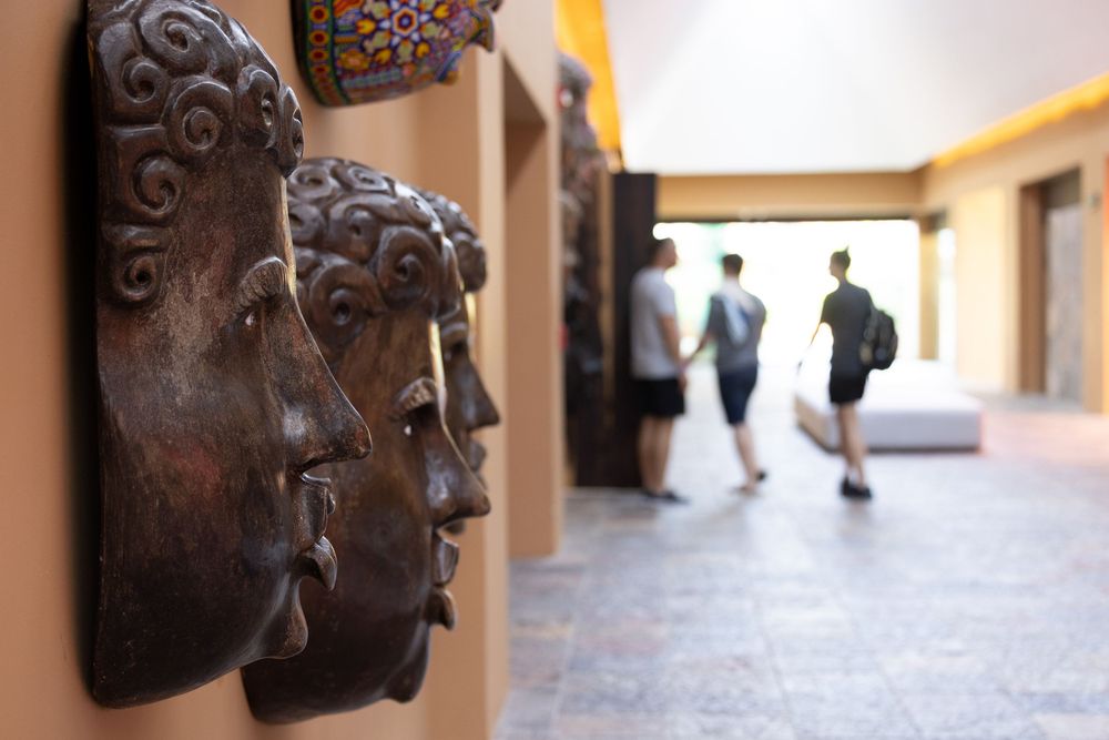Bronze Buddha face masks displayed on a wall in a resort corridor with guests walking in the background.