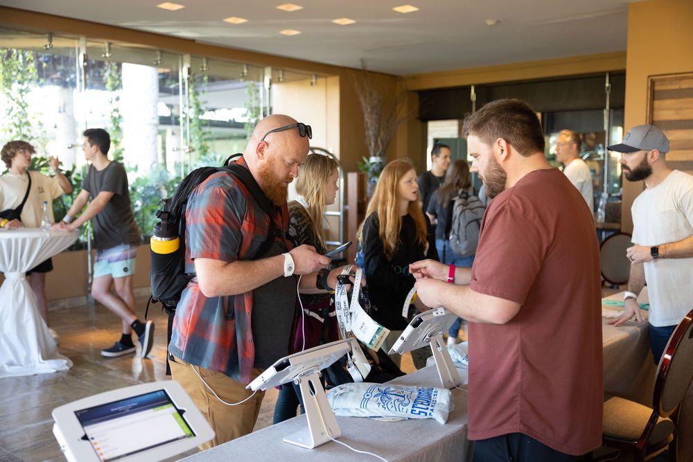 People networking at an indoor event, examining products at a registration table in a modern venue.