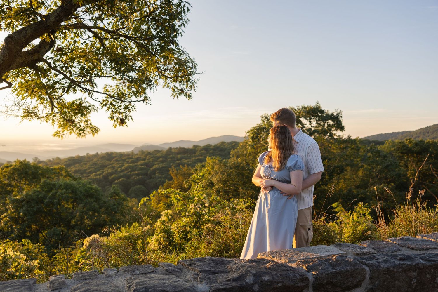 Couple embracing at sunset overlooking lush green rolling hills from a rocky overlook.