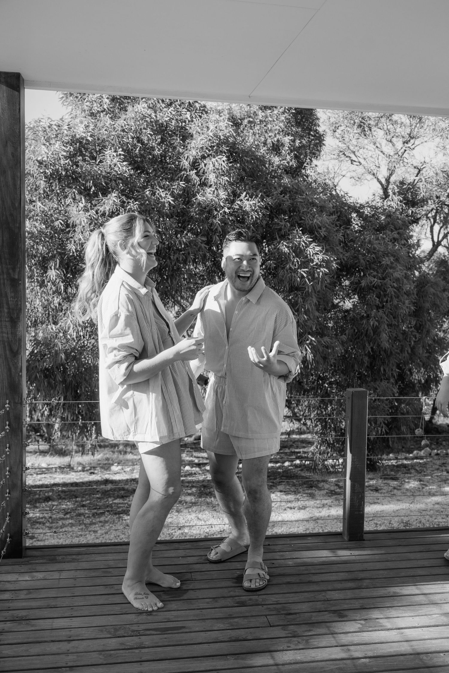 Happy couple laughs together on wooden deck in matching outfits in black and white photo.