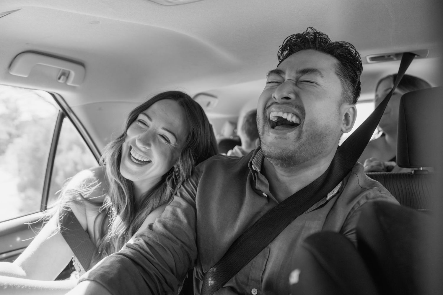 Laughing couple sharing a joyful moment together inside a car in a black and white candid photo.