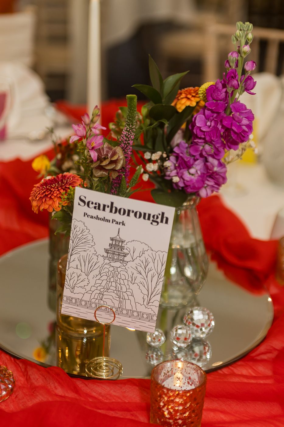 Scarborough Peasholm Park wedding table centerpiece with colorful flowers, mirror base, and red tablecloth decor.