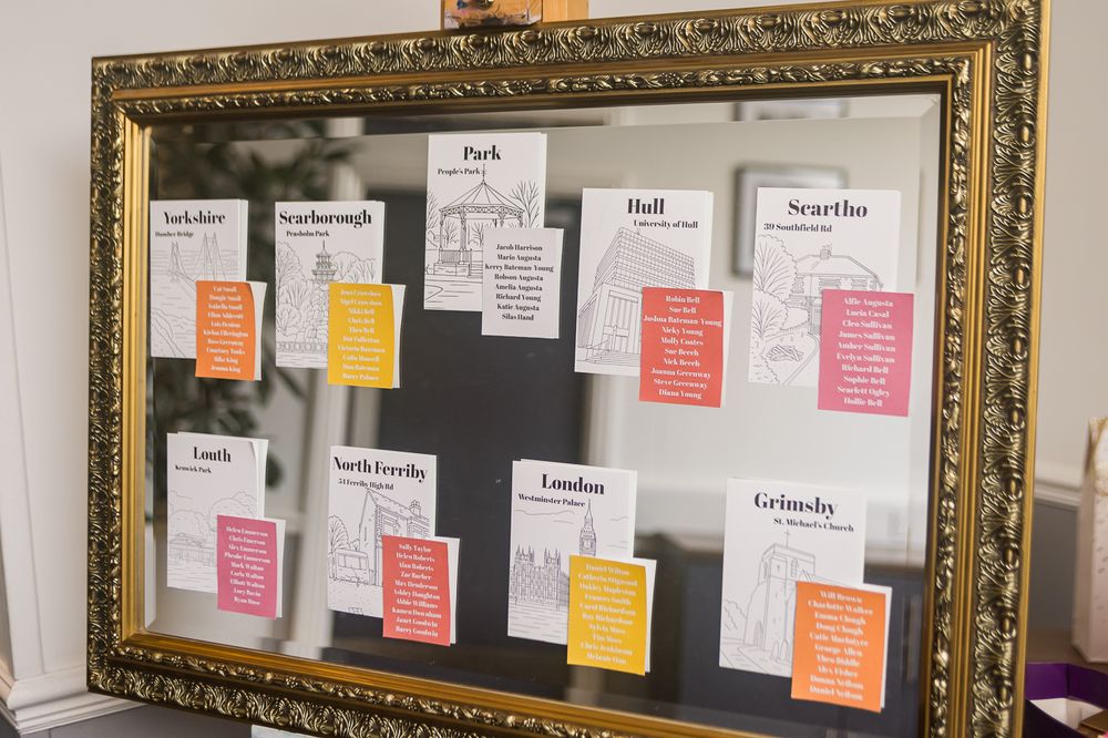Ornate gold framed wedding seating chart with colorful name cards arranged on a mirror display.