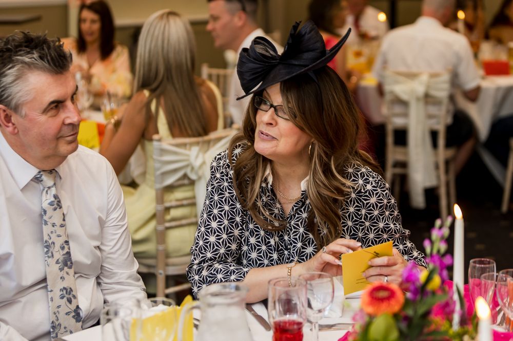 Elegantly dressed woman wearing a black fascinator hat and glasses at a formal dining event.