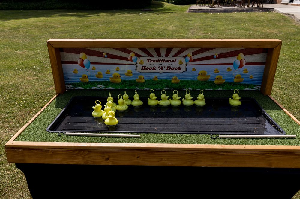 Traditional Hook A Duck fairground game with yellow rubber ducks in a wooden water tray, set outdoors on green grass.