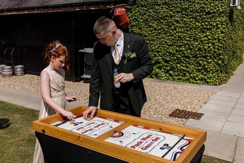 Bride and groom playing shuffleboard game outdoors at wedding venue on sunny day.