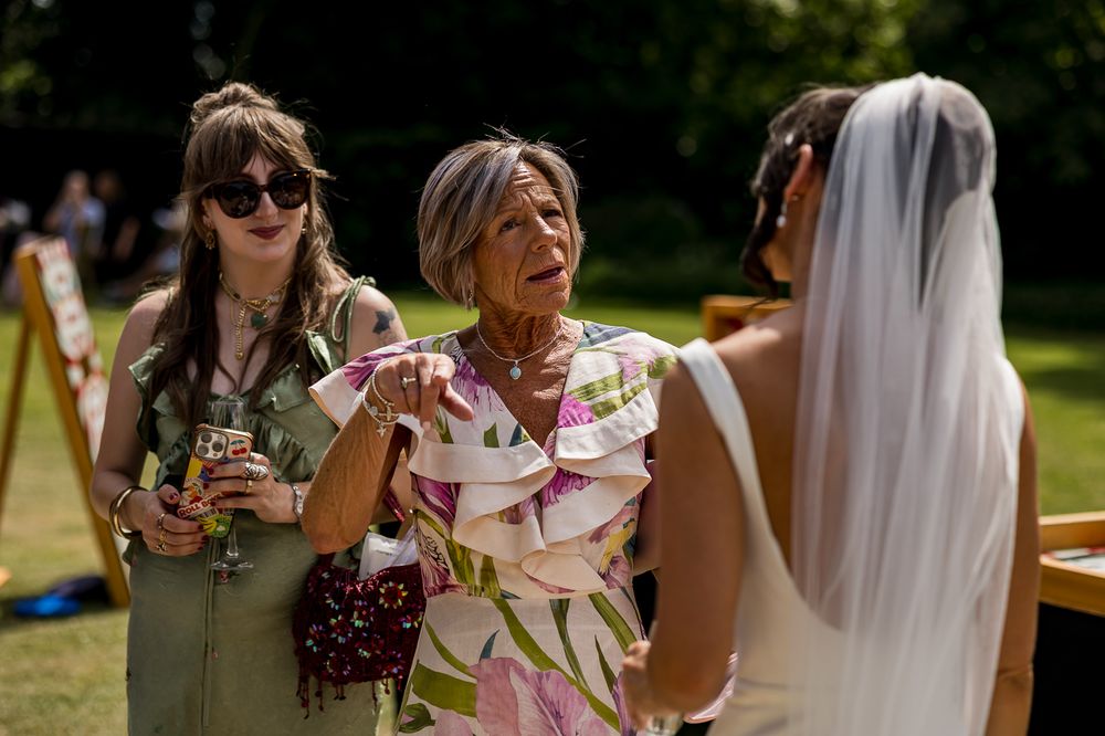 Bride in white veil greeted by guests in colorful dresses at an outdoor wedding celebration.