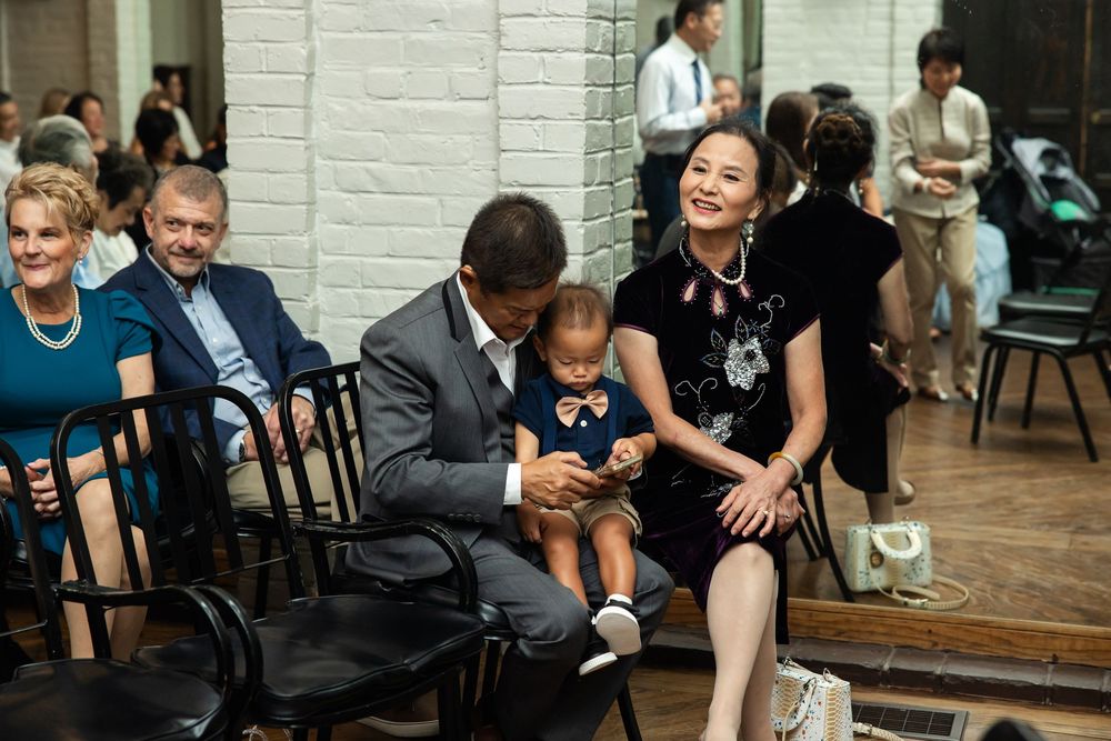 Family gathering indoors with adults and a baby seated on chairs, smiling and interacting in a bright social setting.