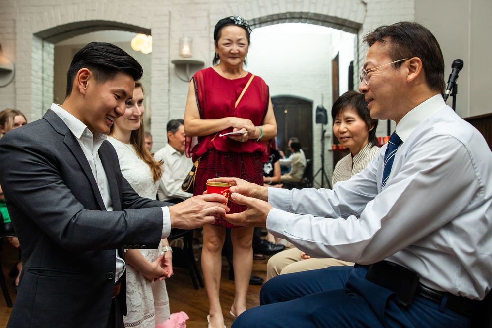 Asian wedding guests exchanging gifts during a traditional tea ceremony celebration indoors.