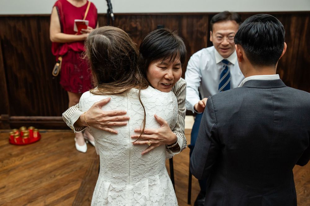 Emotional wedding moment as a woman in white lace dress receives a heartfelt hug from an older woman at a reception.