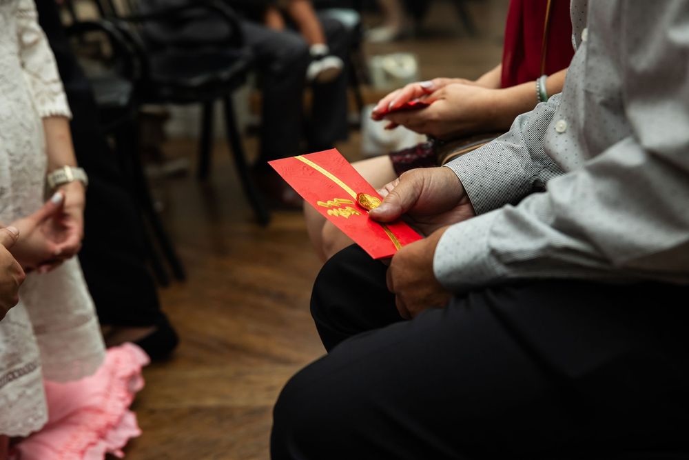Guests holding red envelopes during a traditional Chinese wedding ceremony indoors.