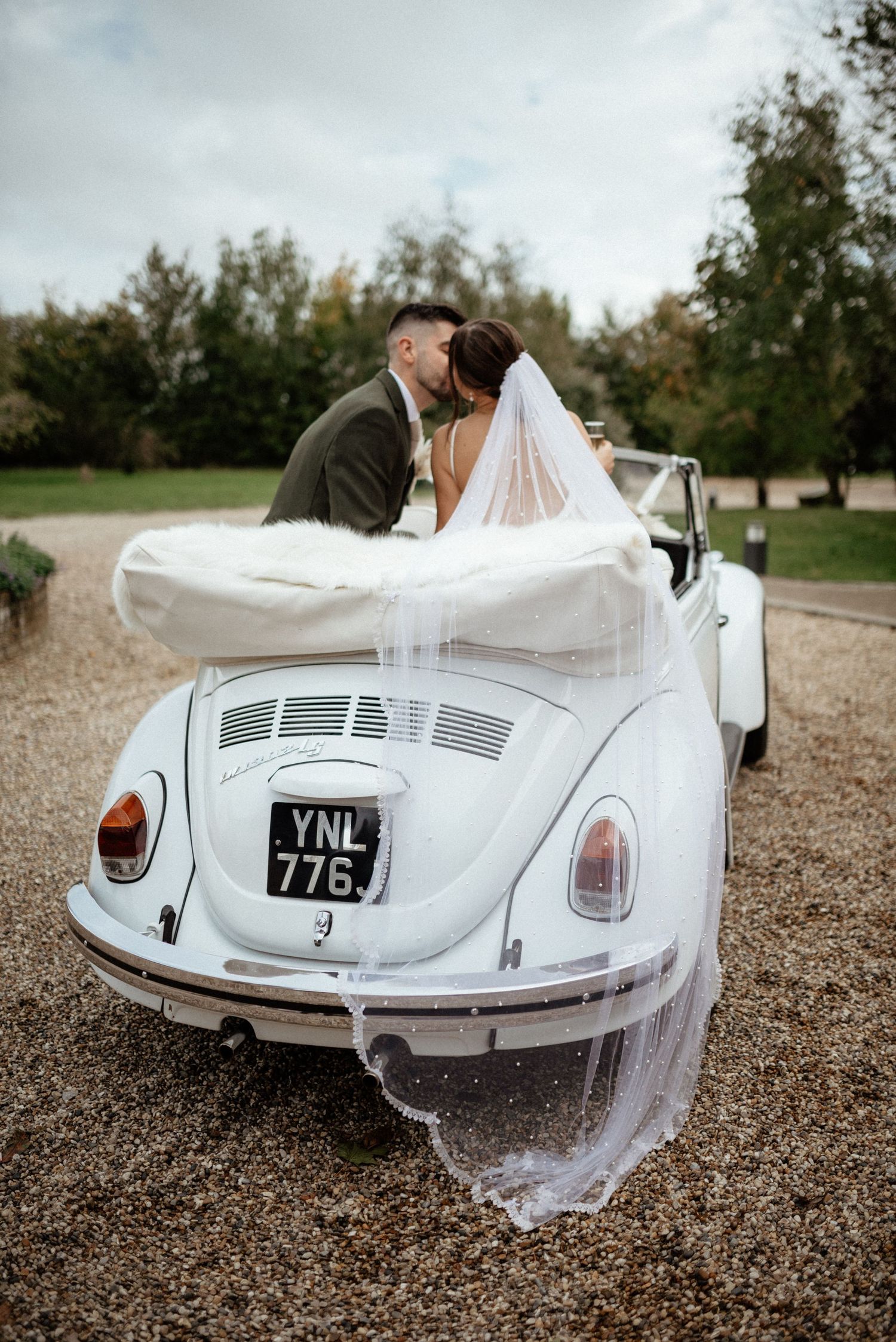 Classic white Volkswagen Beetle decorated with wedding veil on gravel road.