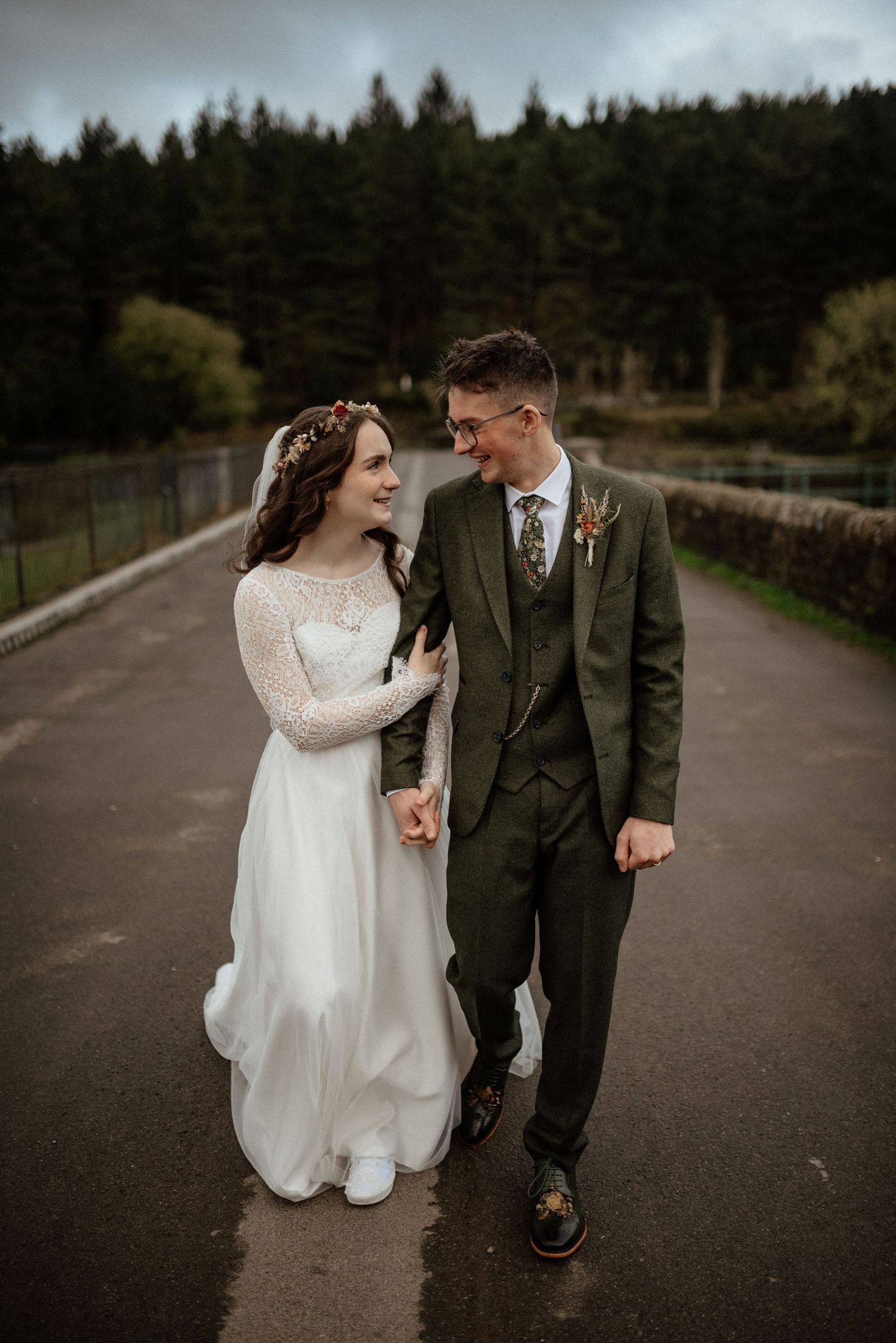 A couple walks together on a moody forest path during their wedding day.