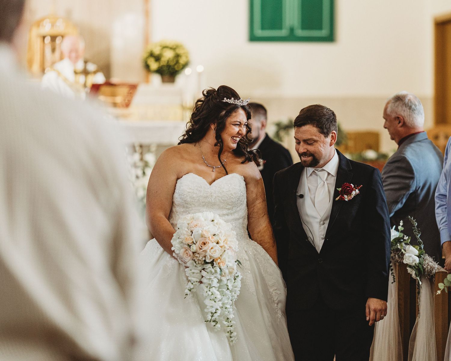 Newlyweds smiling as they walk down the church aisle together after their ceremony.