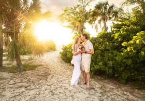 Couple embracing on a sandy tropical path surrounded by palm trees and lush greenery at golden sunset.