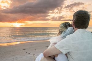 Couple embracing on a sandy beach watching a vibrant sunset over the ocean with colorful clouds in the sky.
