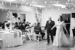 Black and white photo of a bride and groom entering their wedding reception hall filled with seated guests.