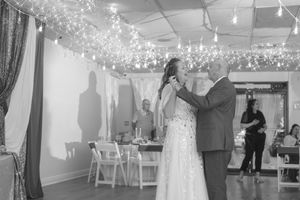 Black and white photo of a bride and groom sharing their first dance under twinkling fairy lights at a wedding reception.