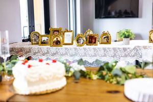 Elegant wedding reception table with gold photo frames, lace tablecloth, white cake, and greenery decor.