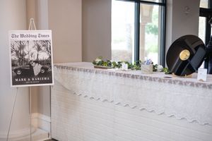 Elegant wedding reception entrance with a custom Wedding Times newspaper sign displaying the couple's names, Mark and Kariema.