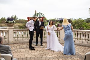 Outdoor wedding ceremony on a stone terrace with bride, groom, officiant, and bridesmaid in blue dress.