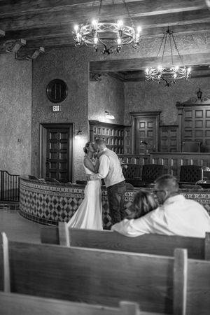 Black and white photo of a couple sharing a kiss at the altar inside a rustic courthouse wedding venue.