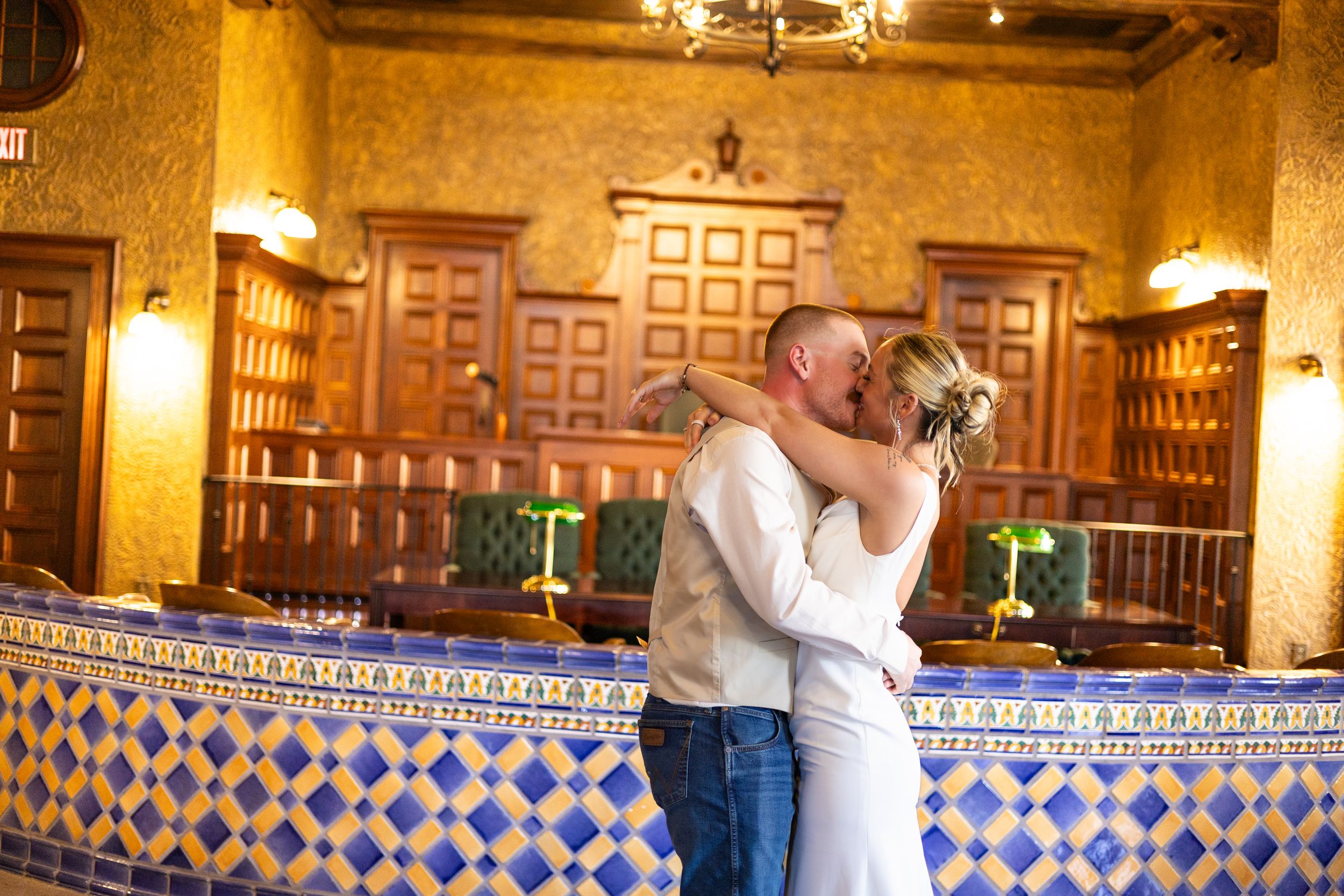 Couple sharing a romantic first kiss at their wedding ceremony in an ornate Spanish-style venue with blue tile accents.