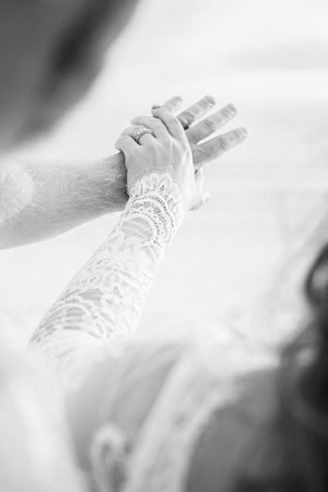 Black and white photo of bride in lace glove holding groom's hand with wedding ring visible at ceremony.