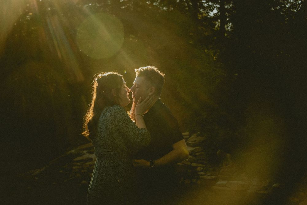 Couple sharing a romantic moment in golden sunlight filtering through trees in a lush outdoor setting.