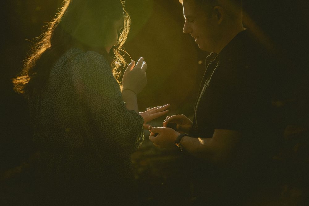 Two people sharing an intimate moment in warm golden light, exchanging a ring in a romantic outdoor setting.