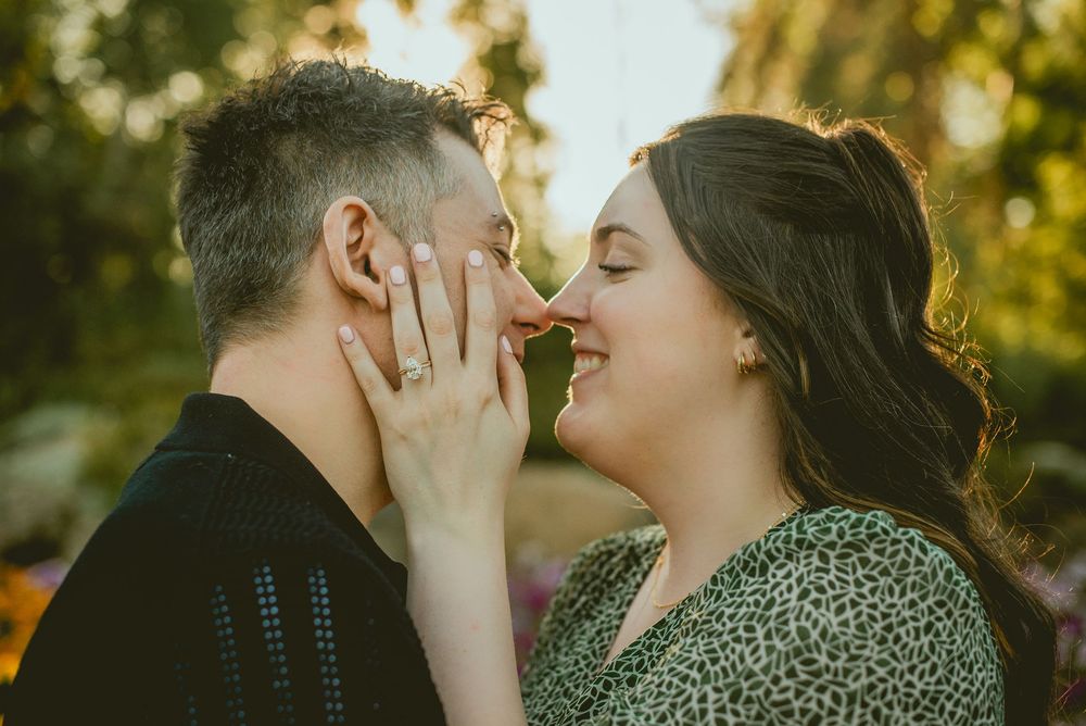 Couple shares a romantic moment, woman showing off engagement ring while almost kissing.
