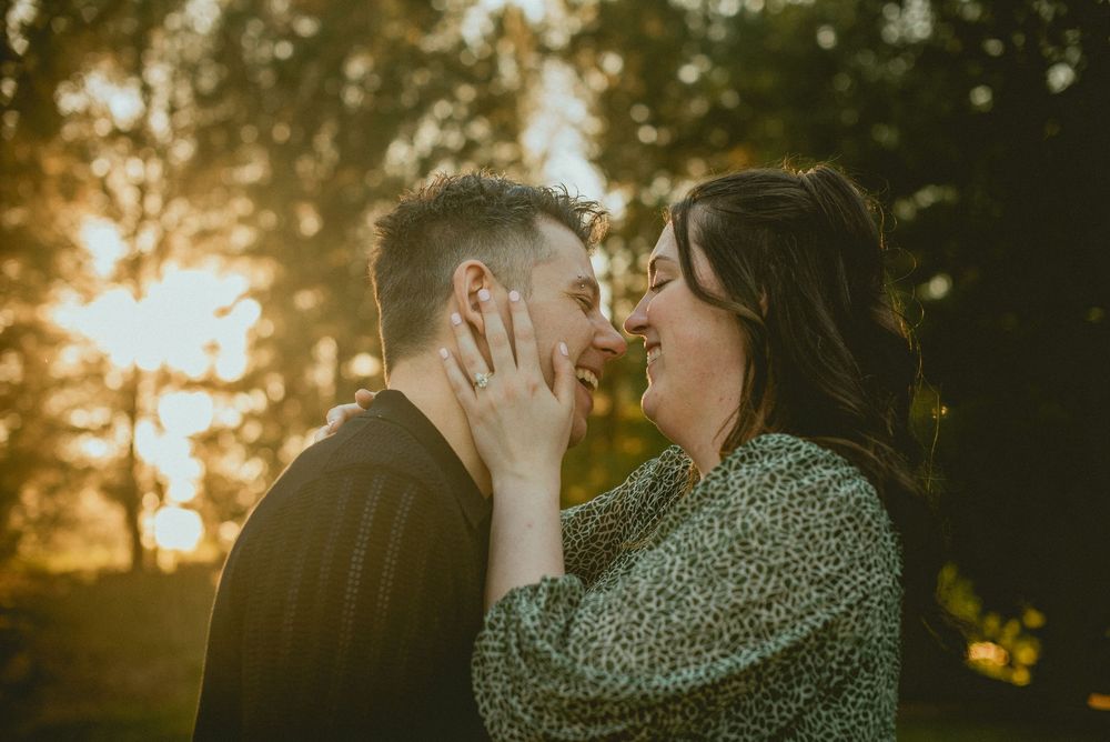 Couple sharing a romantic moment at golden hour, surrounded by glowing sunlight and lush green trees.