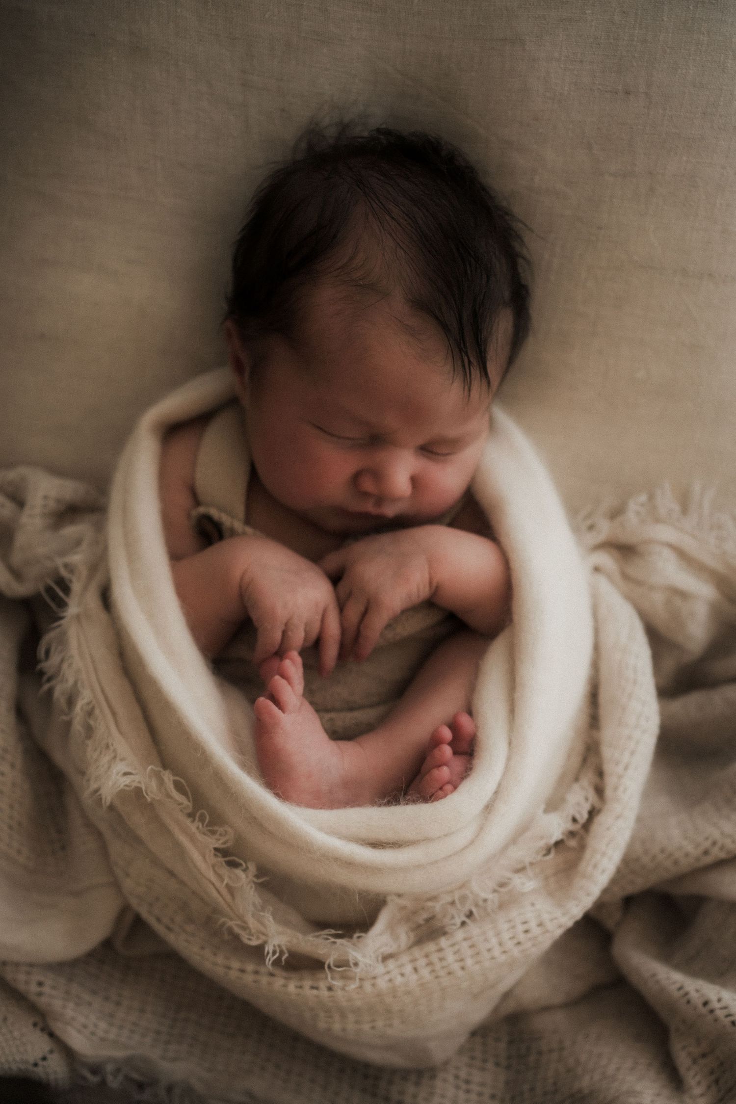 Newborn baby sleeping peacefully wrapped in a soft cream knit blanket with tiny feet visible photographed in Buxton, Victoria