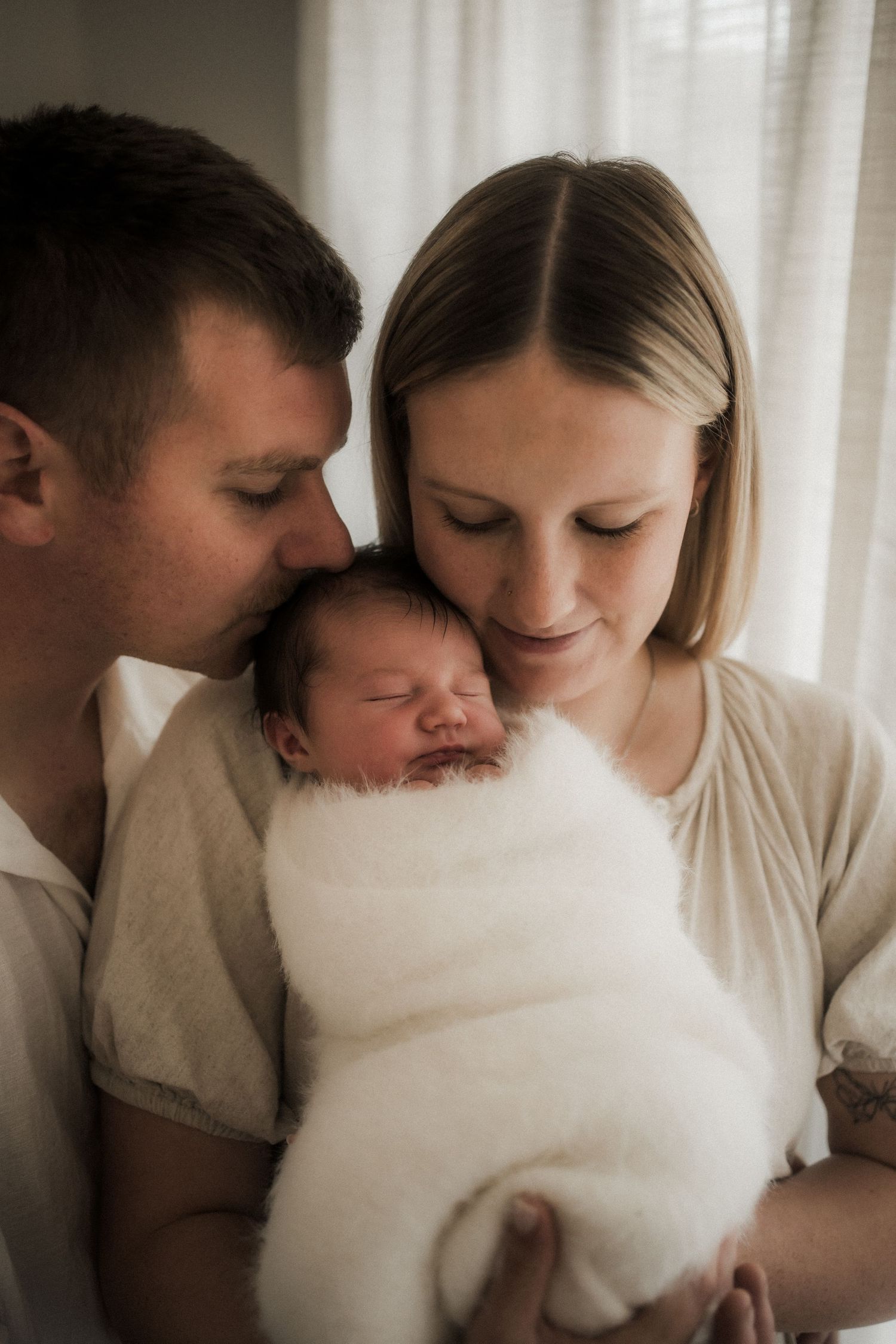 New parents tenderly hold their sleeping newborn wrapped in white, sharing a precious family moment in the Yarra Valley, Victoria