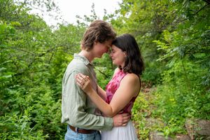 A young couple embraces tenderly in a lush green forest setting, sharing a romantic moment outdoors.